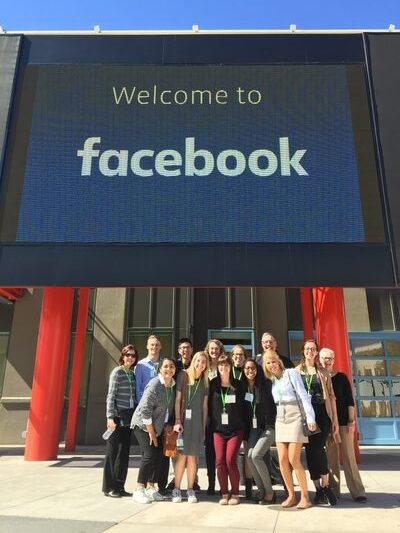a group of students standing in front of a digital sign that reads "welcome to Facebook."