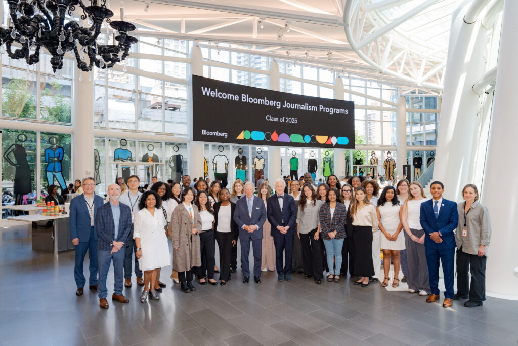 a group of students and advisers stand in the Bloomberg lobby. There is a sign in the background that reads "Welcome to the Bloomberg Journalism Diversity Program." 2025