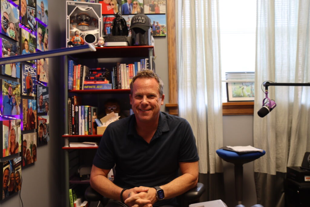 a man sits in his office, which is decorated with family photos and Star Wars collectibles