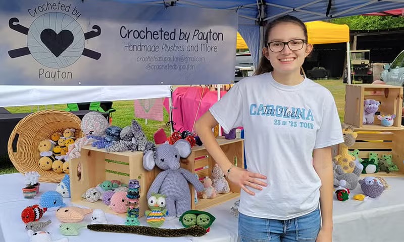 a young woman stands in front of a table that is covered in crocheted animals