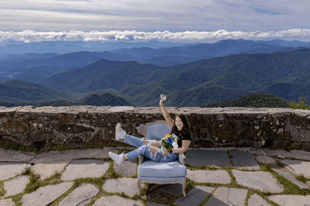 a woman sits in a blue arm chair that is situated on a mountain lookout.