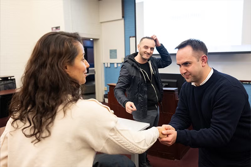 a woman and man shake hands, and another man stands behind them
