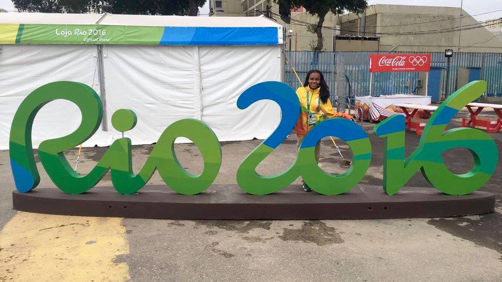 a woman stands behind giant letters that read "Rio 2016"
