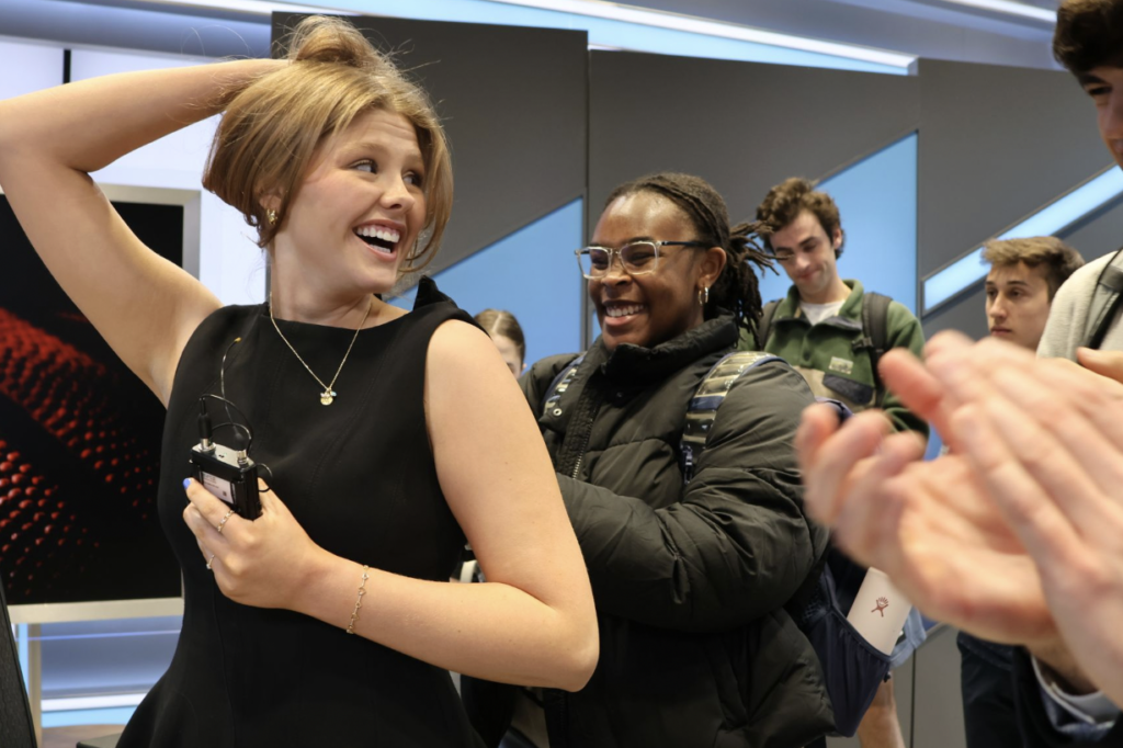 a woman holds up her hair while another woman hooks her up to a lapel mic