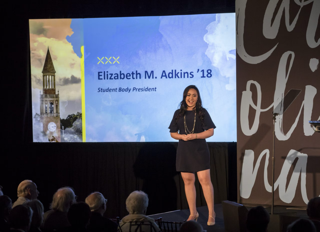 Elizabeth Adkins stands in front of a screen on stage.