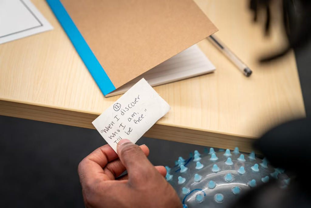 A hand holds a small piece of paper that says When I discover who I am, I'll be free.
