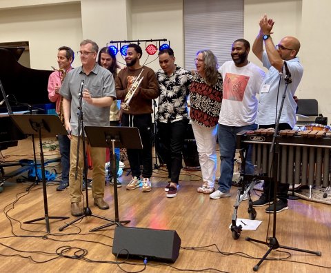 eight musicians pose with instruments in front of microphones and music stands